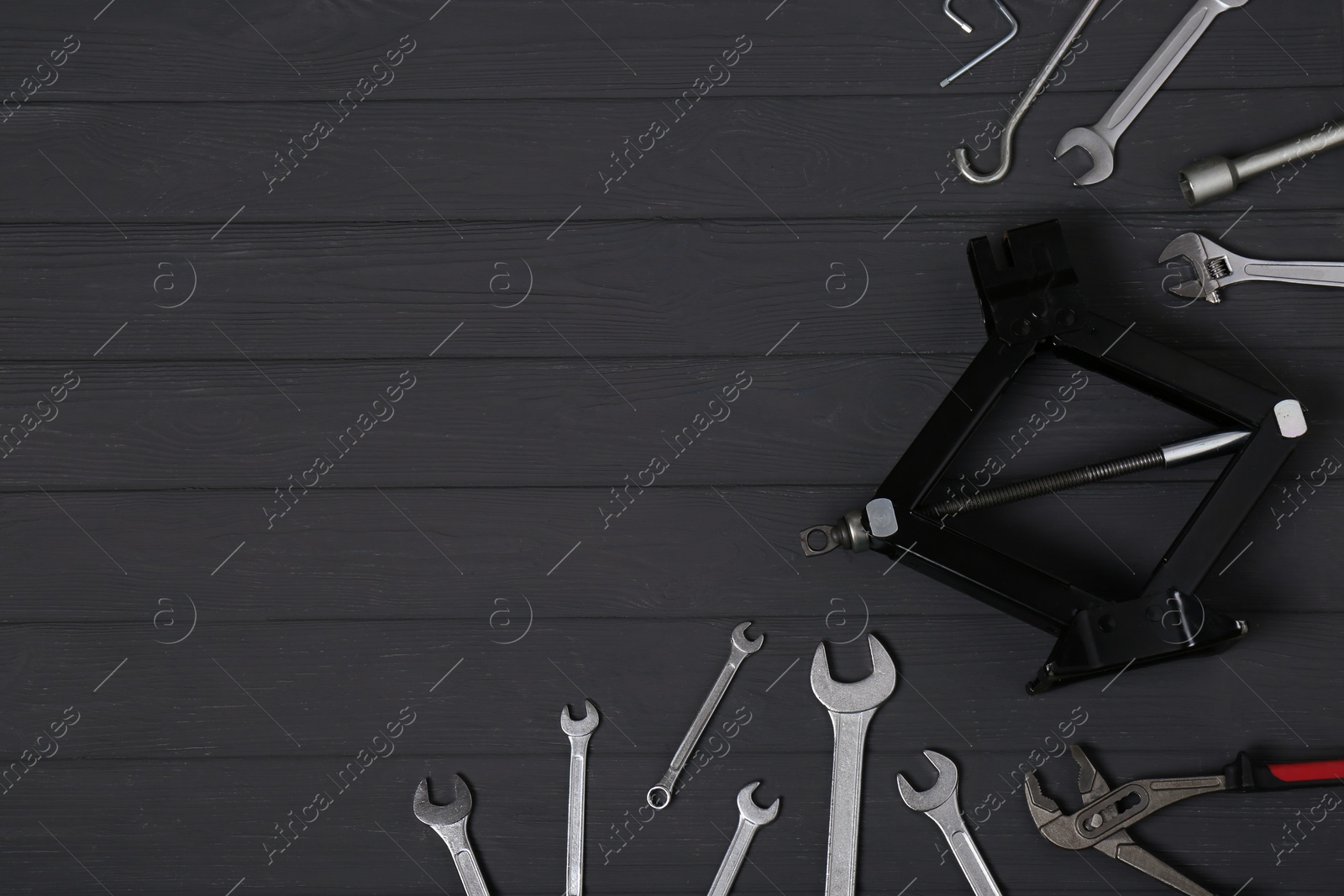 Photo of Car scissor jack and wrench set on black wooden surface, flat lay. Space for text
