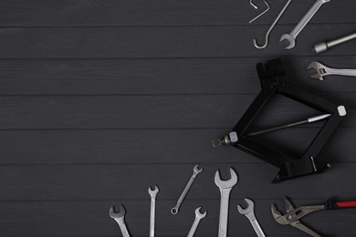 Photo of Car scissor jack and wrench set on black wooden surface, flat lay. Space for text