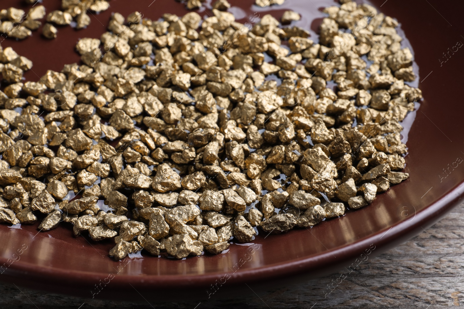 Photo of Plate of gold nuggets on wooden table, closeup