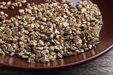 Plate of gold nuggets on wooden table, closeup