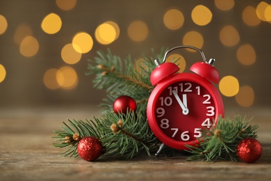 Photo of Alarm clock with decor on wooden table against blurred Christmas lights, closeup. New Year countdown