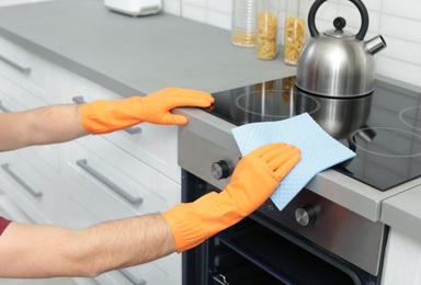 Young man cleaning oven with rag in kitchen, closeup