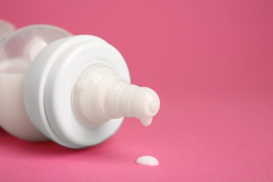Feeding bottle with milk on pink background, closeup. Space for text
