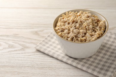 Photo of Tasty boiled oatmeal in bowl on light wooden table, space for text