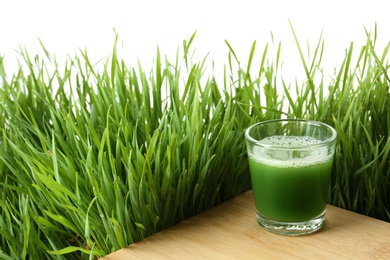 Photo of Glass of juice on table and fresh wheat grass against white background. Space for text