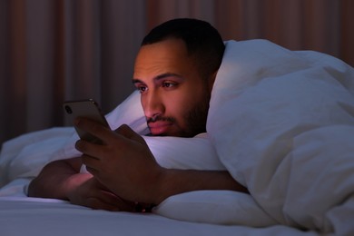 Young man using smartphone under blanket in bed at night. Internet addiction