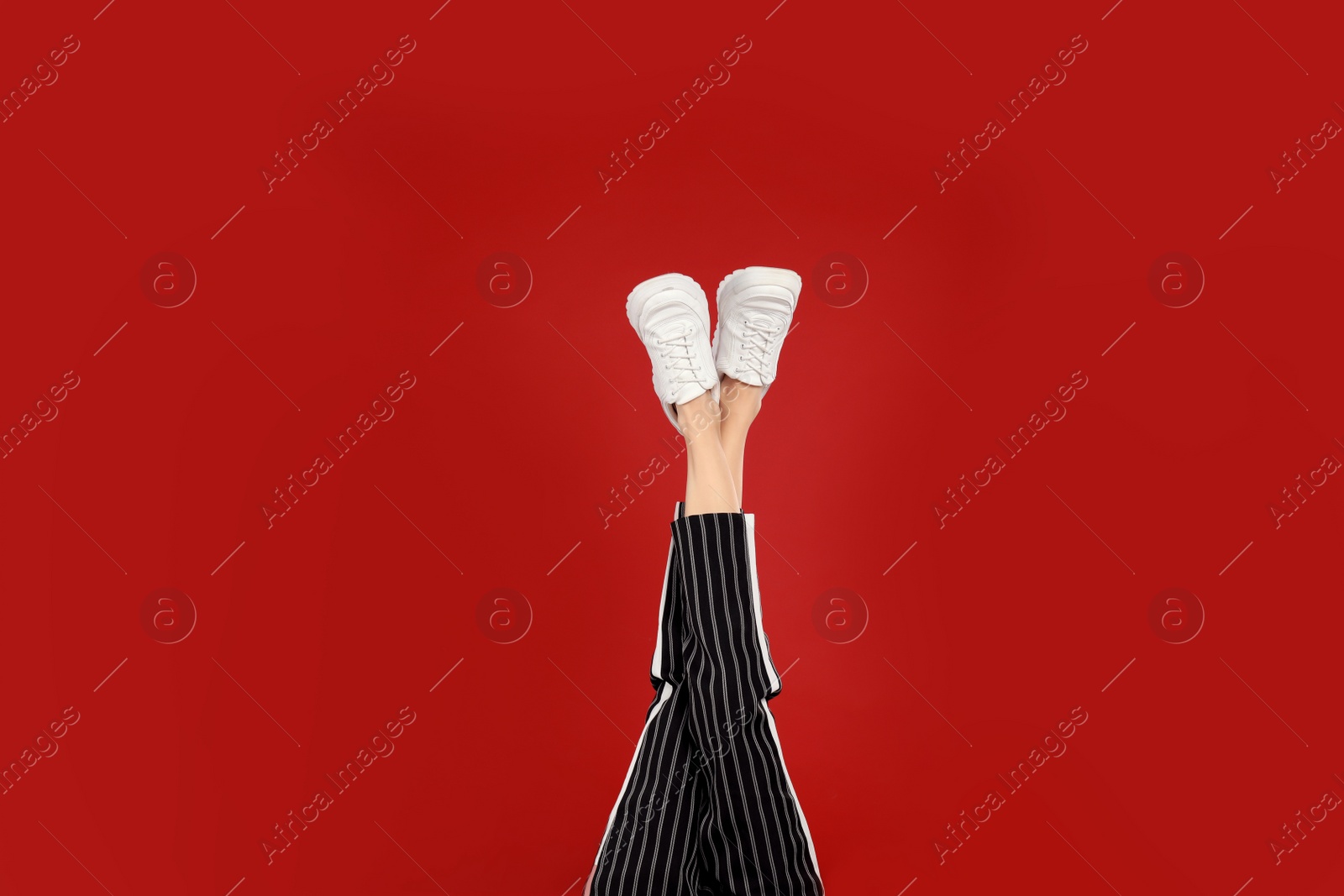 Photo of Woman in stylish sport shoes on red background