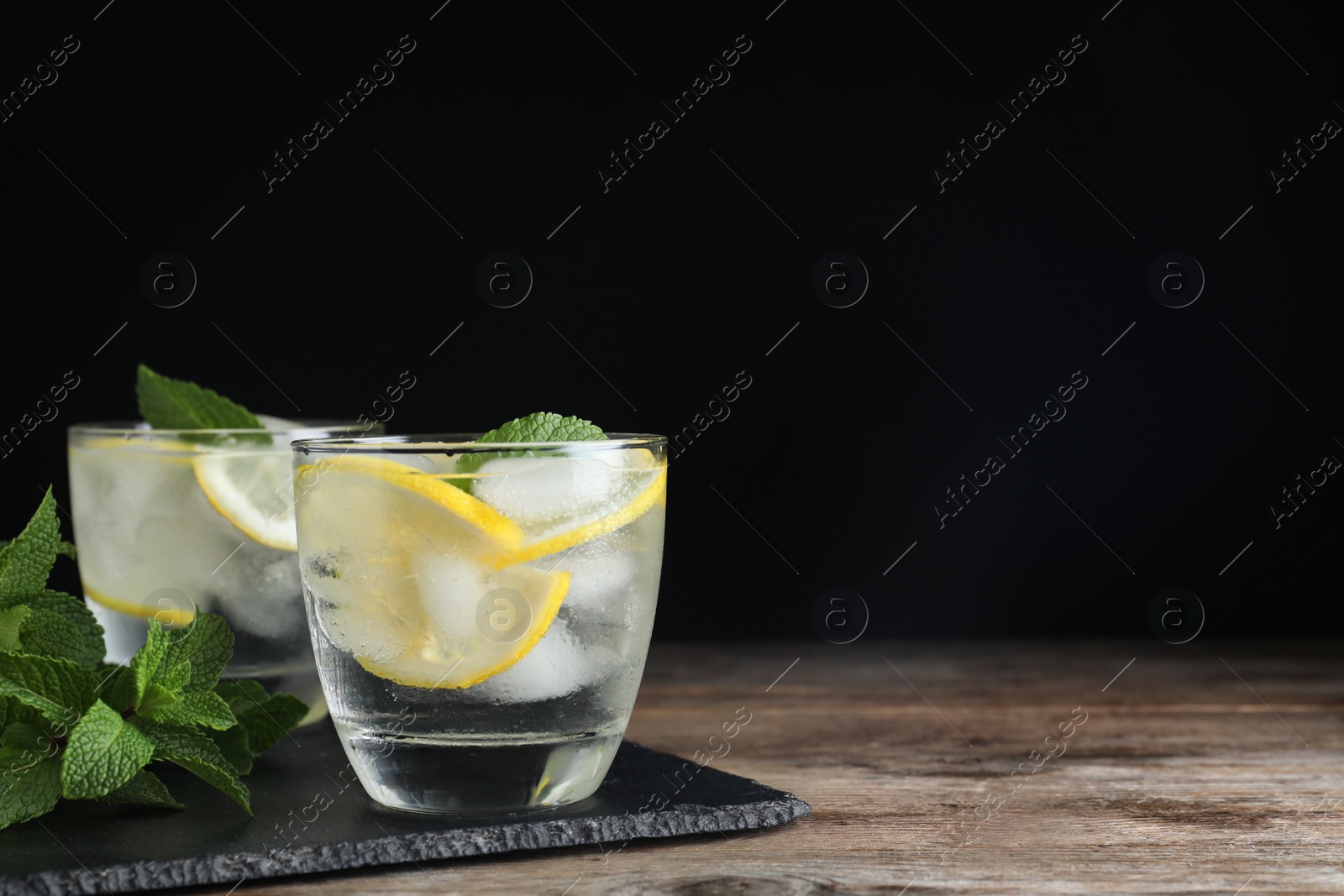 Photo of Glass of cocktail with vodka, ice and lemon on wooden table against black background. Space for text