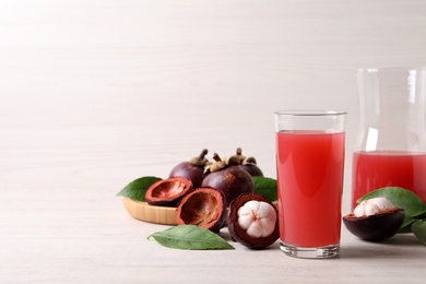 Photo of Delicious mangosteen juice and fresh fruits on white table. Space for text