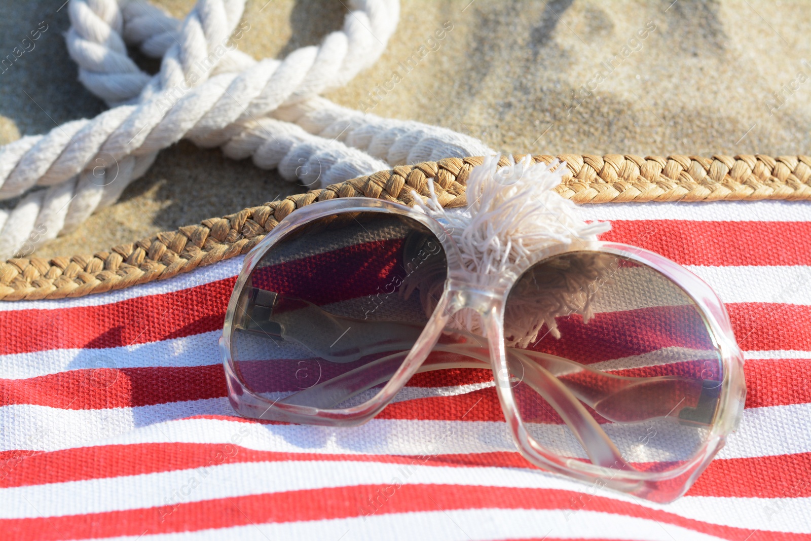 Photo of Stylish sunglasses and beach bag on sand, closeup