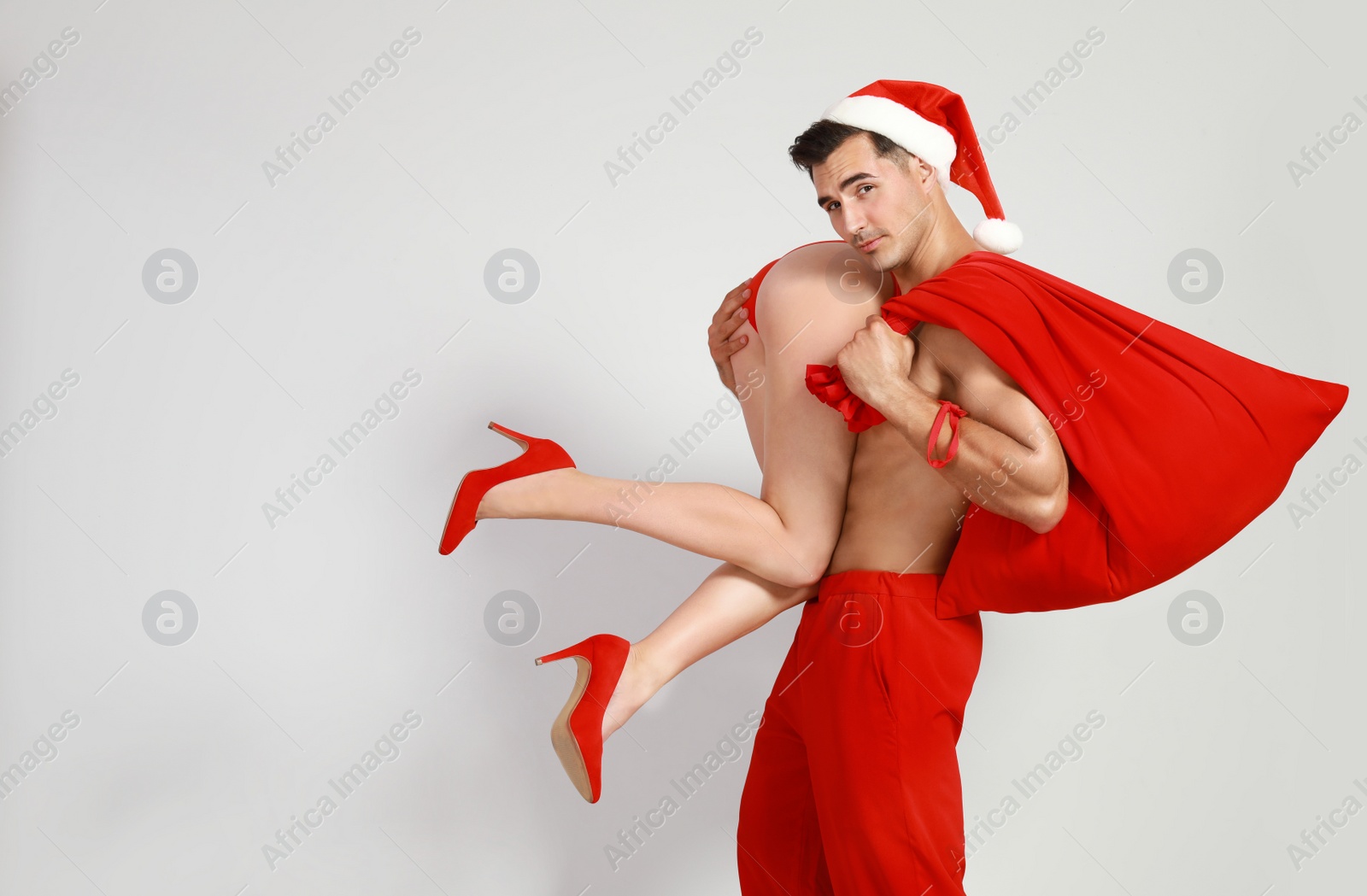 Photo of Attractive young Santa Claus with sexy woman on light background. Space for text