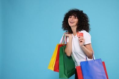 Happy young woman with shopping bags and credit cards on light blue background. Space for text