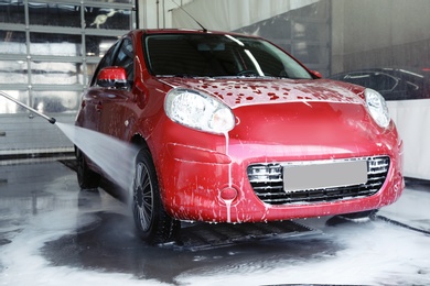 Cleaning modern automobile with high pressure water jet at car wash