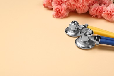 Photo of Stethoscopes and beautiful flowers on beige background, space for text. Happy Doctor's Day