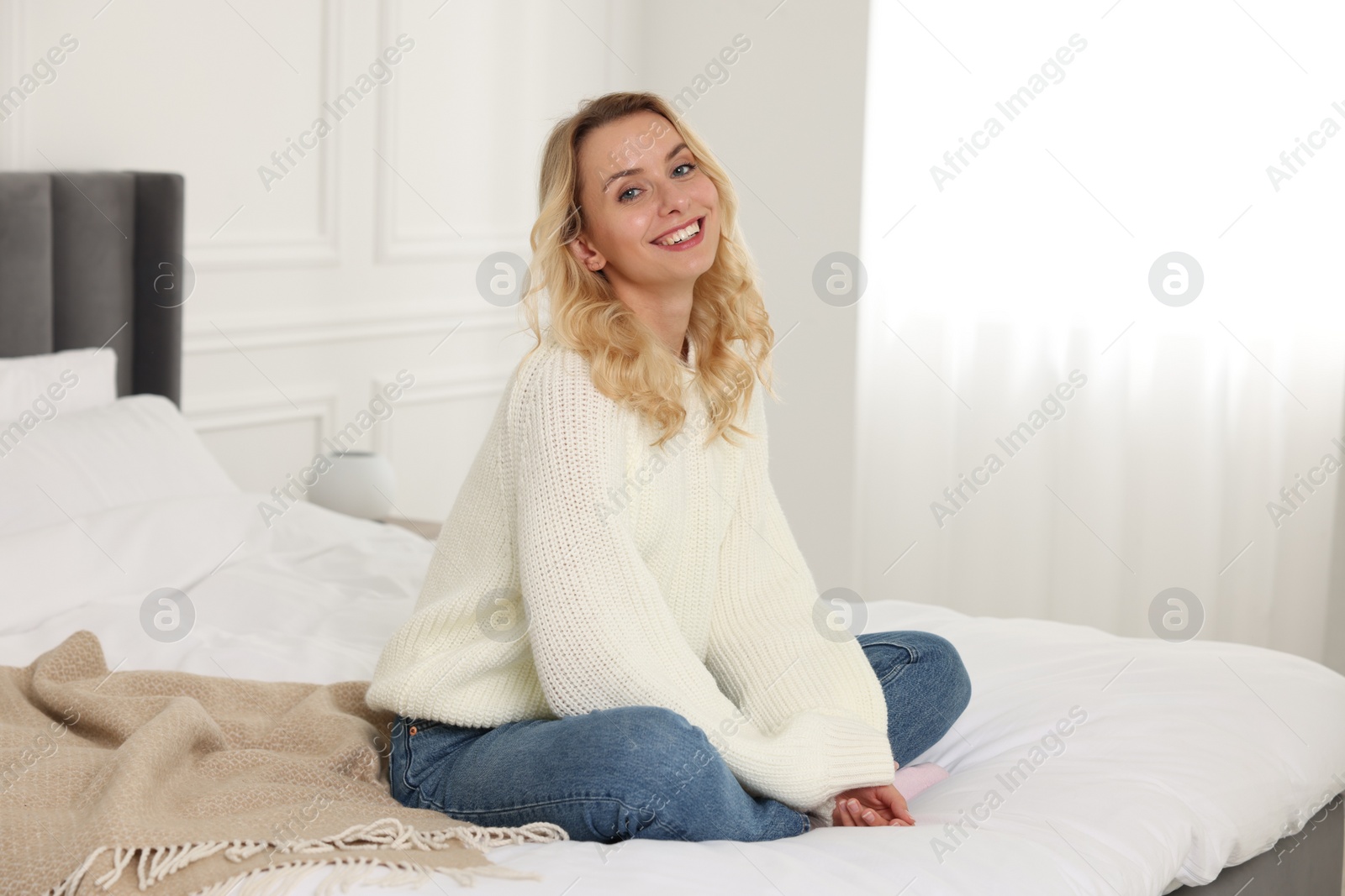 Photo of Happy woman in stylish warm sweater on bed at home