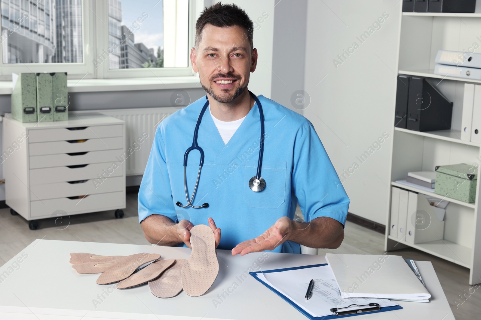 Photo of Handsome male orthopedist showing insoles in hospital