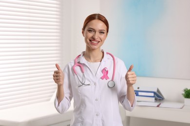 Mammologist with pink ribbon showing thumbs up in hospital. Breast cancer awareness