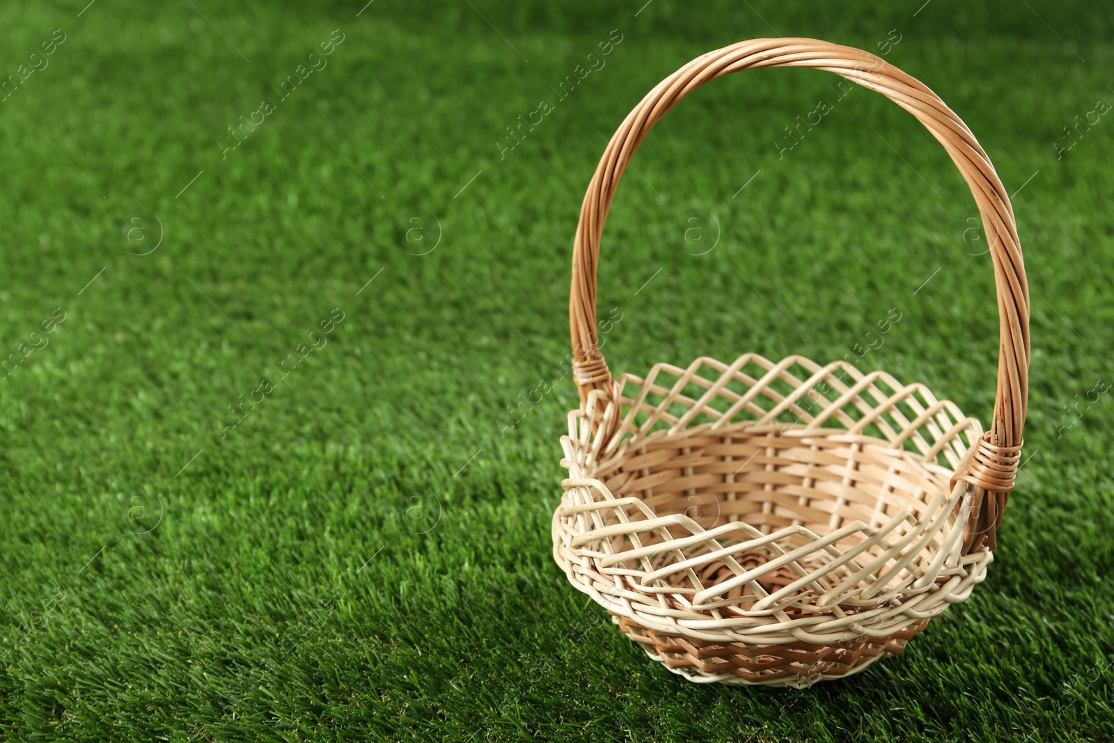 Photo of Empty wicker basket on green lawn, space for text. Easter item