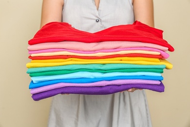 Photo of Woman holding stack of colorful t-shirts on light background