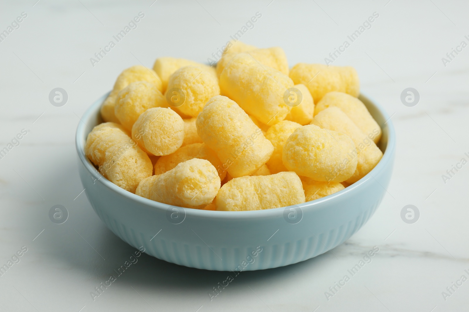 Photo of Bowl of delicious crispy corn sticks on white marble table