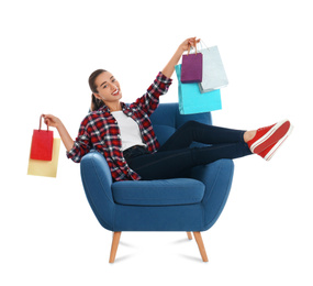 Young woman with shopping bags sitting in armchair on white background