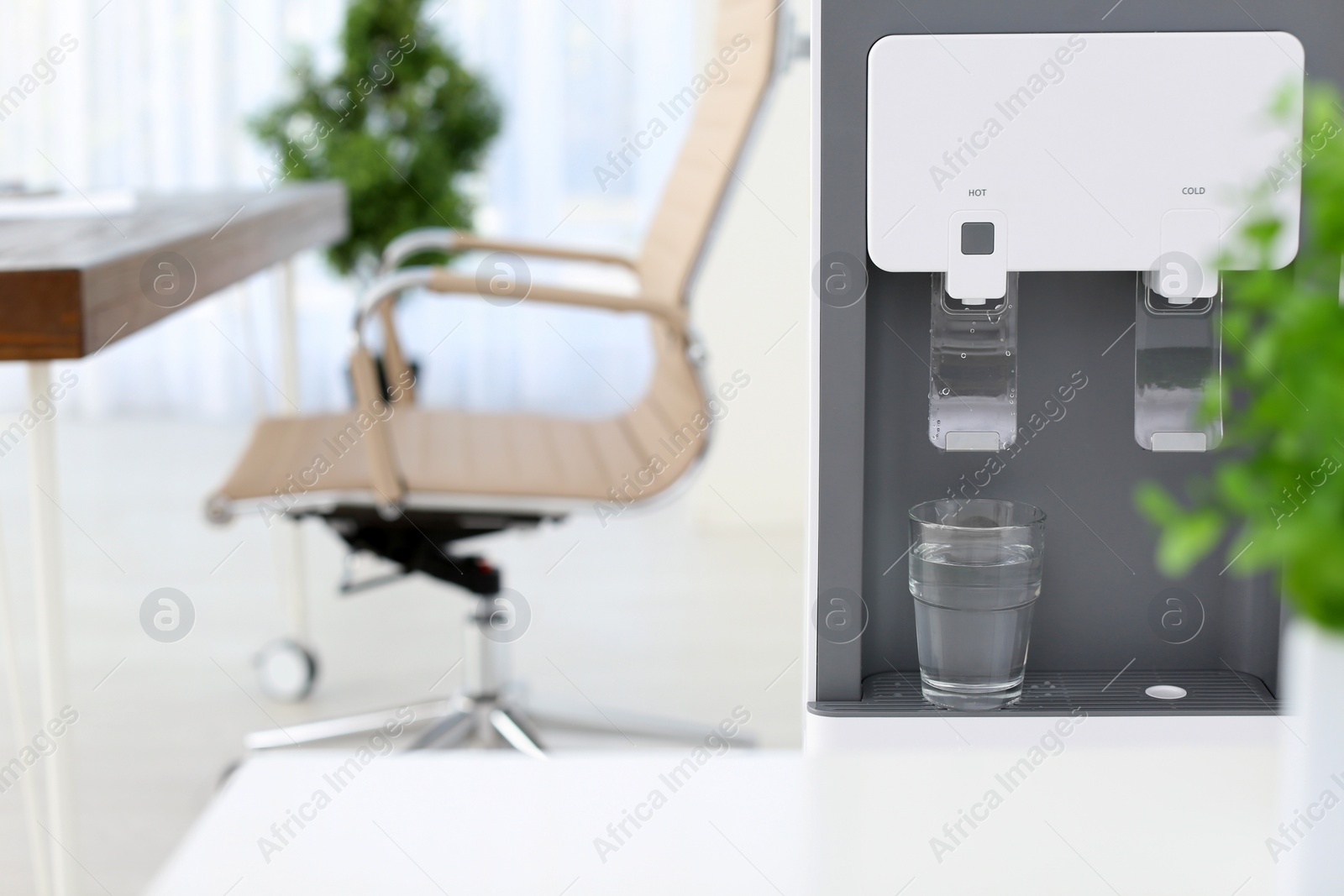 Photo of Modern water cooler with glass in office. Space for text