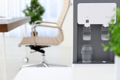 Modern water cooler with glass in office. Space for text