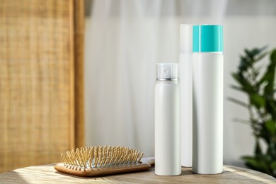 Photo of Bottles of dry shampoos and hairbrush on wooden table indoors