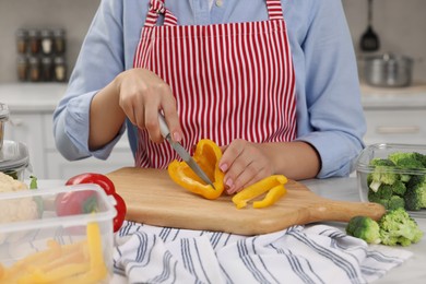 Photo of Woman cutting bell pepper near food storage containers at table in kitchen, closeup