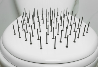 Toilet bowl with nails near marble wall, closeup. Hemorrhoids concept