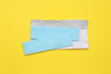 Photo of Sticks of tasty chewing gum on yellow background, flat lay