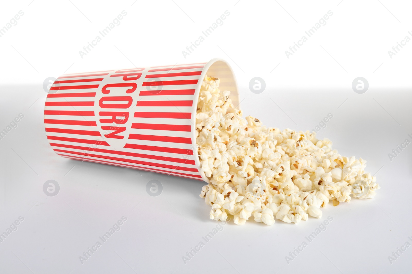 Photo of Overturned paper cup with delicious popcorn isolated on white