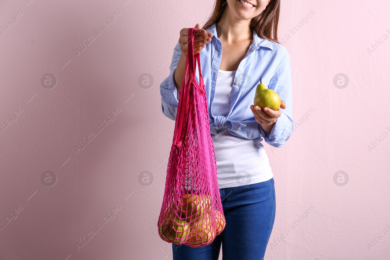 Photo of Woman holding net bag with fresh ripe pears on pink background, closeup