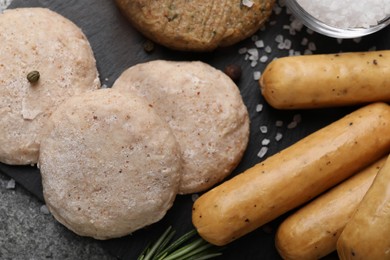 Photo of Different raw vegan meat products, salt and rosemary on dark board, flat lay