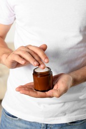 Man holding jar of hand cream, closeup view