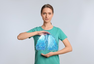 Image of Young woman holding hands near chest with illustration of lungs on light grey background