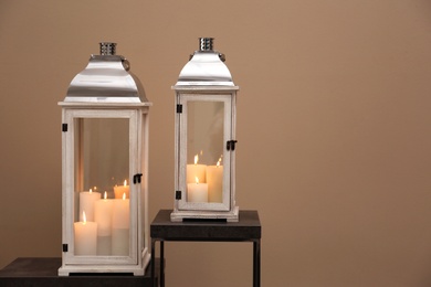 Decorative lanterns with candles on stands against beige background, space for text. Interior elements