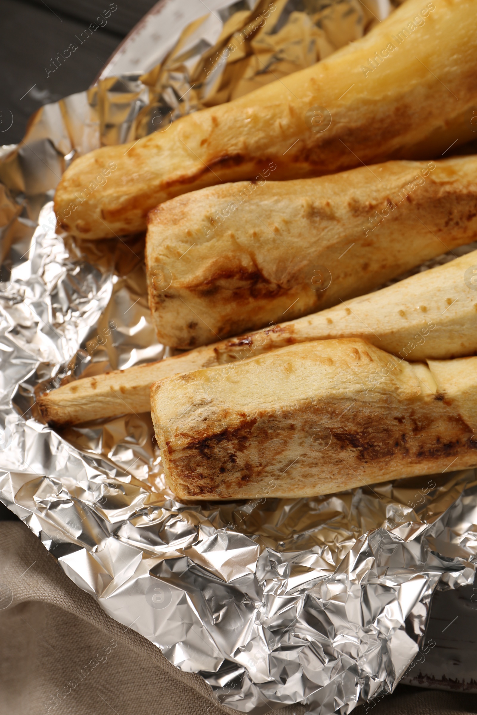 Photo of Plate of tasty baked parsnips on table, closeup