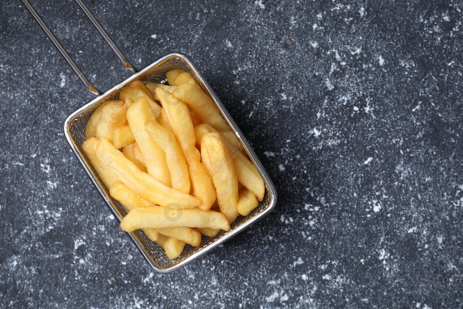 Photo of Metal basket with tasty French fries on black textured table, top view. Space for text