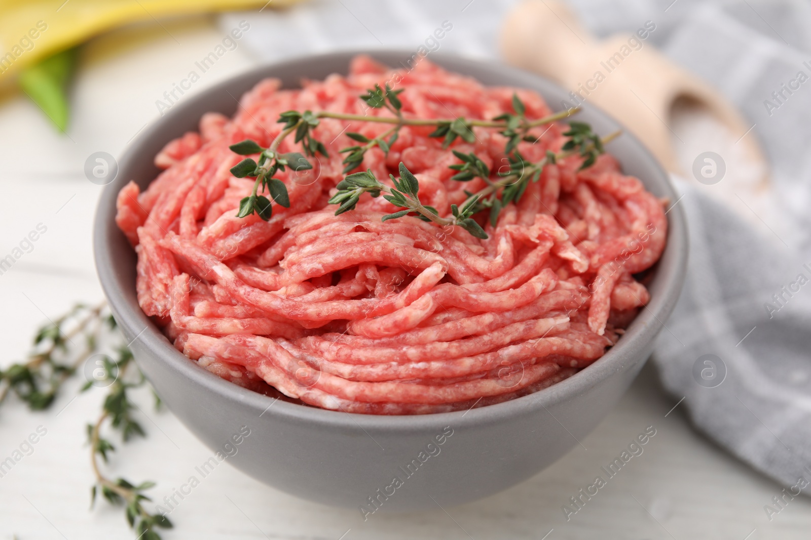 Photo of Fresh raw ground meat and thyme in bowl on white table, closeup