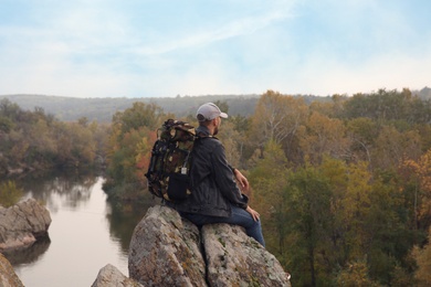 Photo of Hiker with travel backpack sitting on steep cliff near mountain river