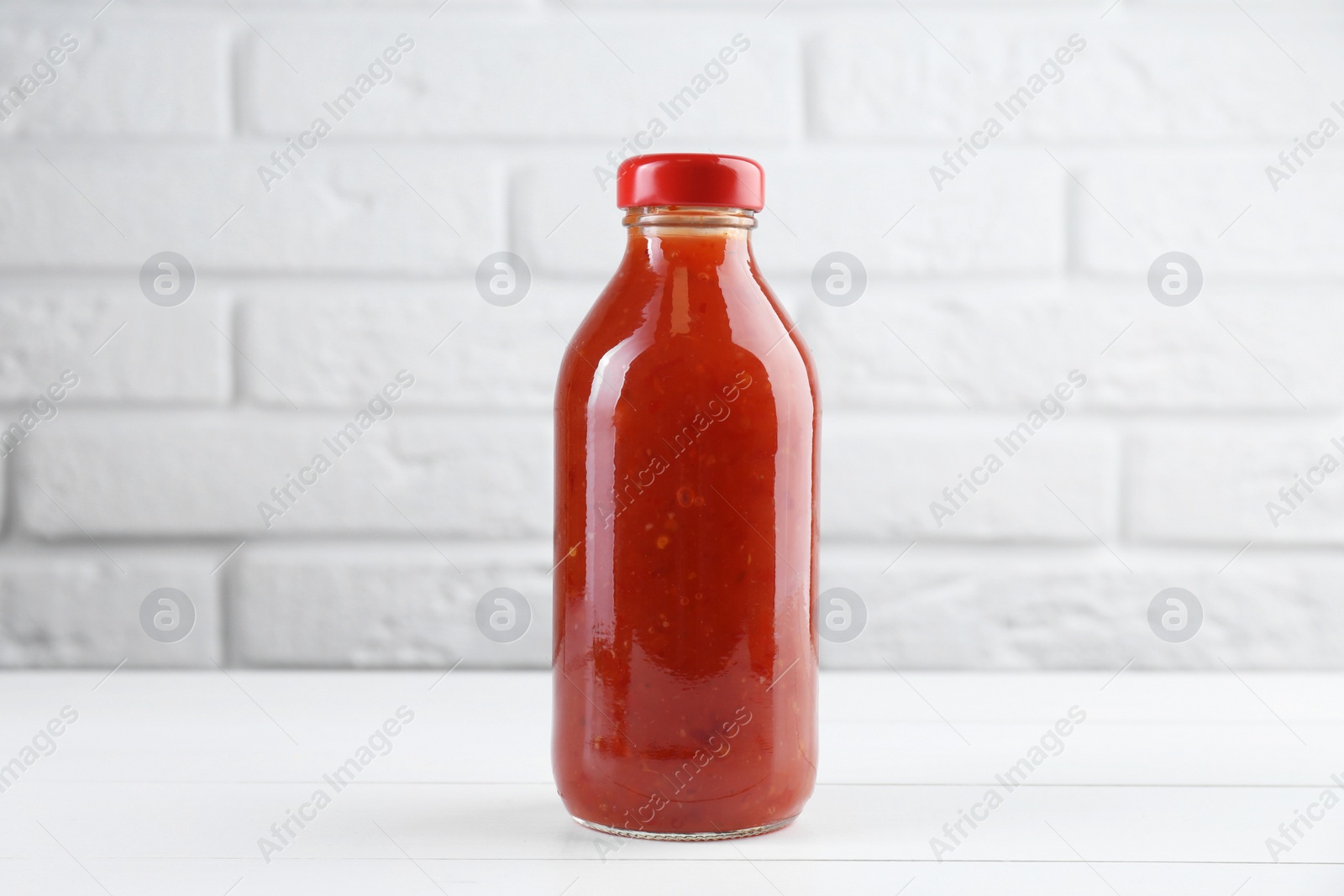 Photo of Spicy chili sauce in bottle on white wooden table