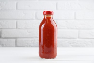 Photo of Spicy chili sauce in bottle on white wooden table