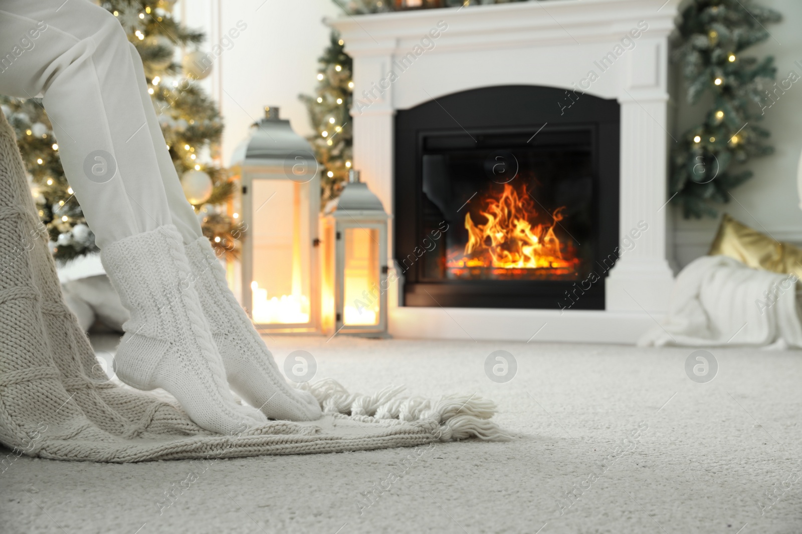 Photo of Woman in knitted socks resting near fireplace at home, closeup