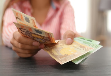 Photo of Woman with Euro banknotes at table indoors, closeup
