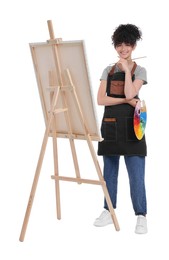 Photo of Young woman holding brush and artist`s palette near easel with canvas against white background