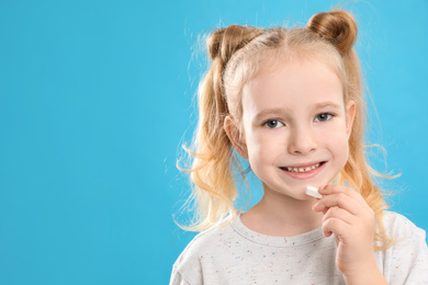 Photo of Little girl taking vitamin pill on light blue background. Space for text