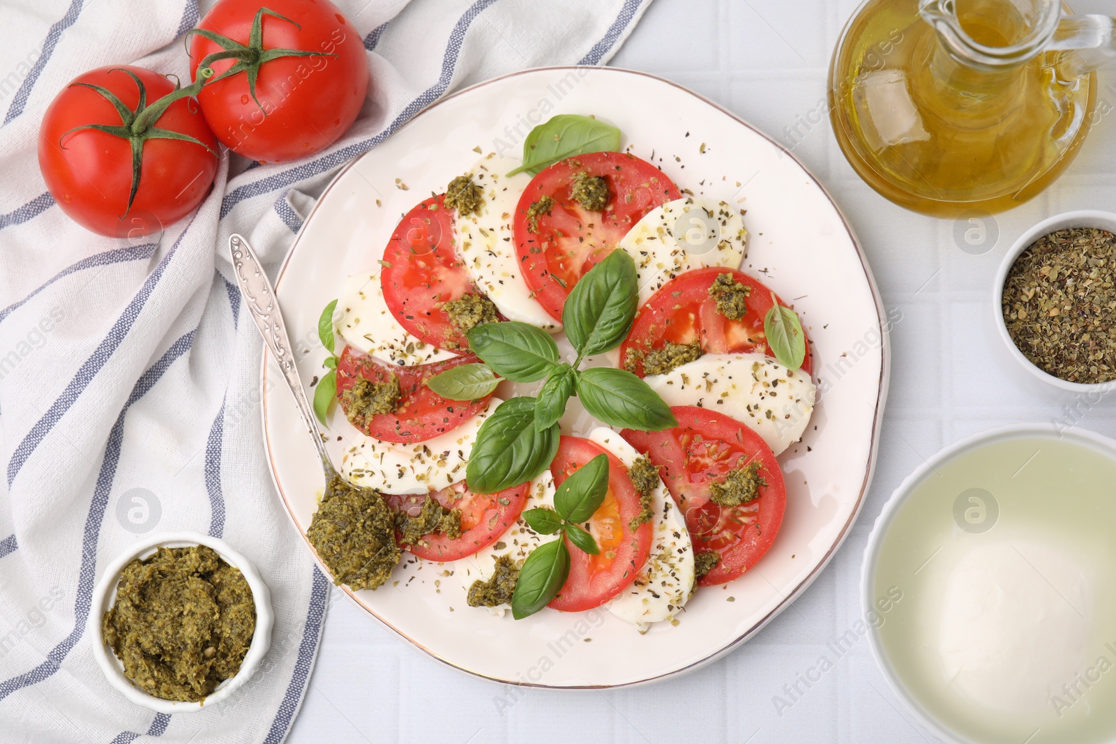 Photo of Plate of delicious Caprese salad with pesto sauce on white tiled table, flat lay