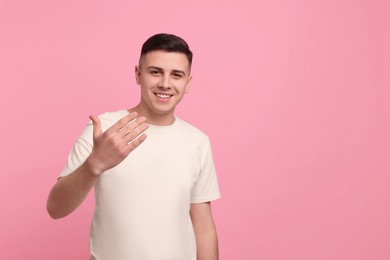 Handsome man inviting to come in against pink background. Space for text