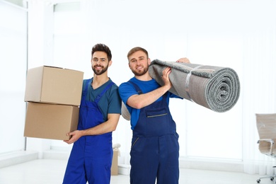 Young workers carrying rolled carpet and boxes in room. Moving service